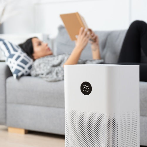 Woman lying on the couch reading a book with an air purifier cleaning the room