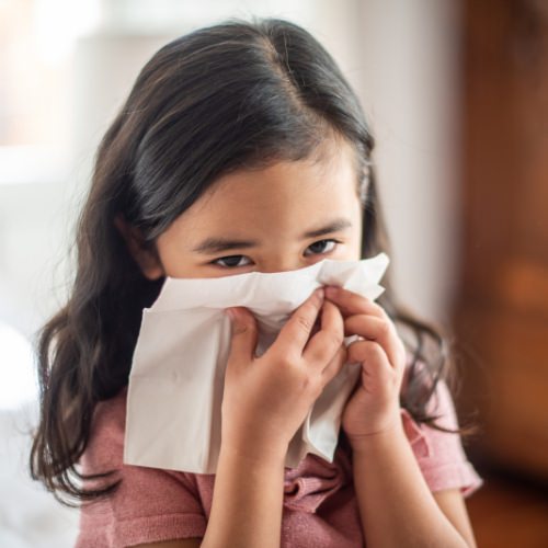 Young girl blowing her nose from allergies caused by dust and dust mites