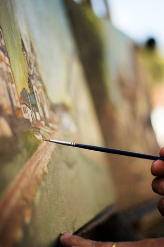 Close-up of an artist's hand painting a detailed scene on canvas, demonstrating the need for a good air purifier for art studios to ensure a clean and safe breathing environment.