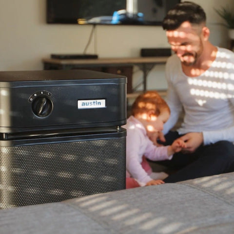 ustin Air Systems Healthmate Plus air purifier in a family room, with a playful father and child in the background.