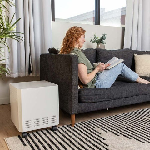 Woman relaxing on sofa reading a book with a white EnviroKlenz Mobile Air System purifier in a cozy living room