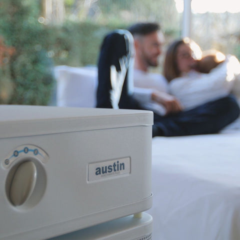 Austin Healthmate Plus 5 air purifier enhancing room ventilation, with a couple relaxing in the blurred background