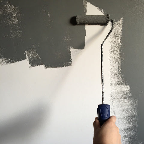 Hand holding a paint roller applying grey paint on a wall, indicative of the need for an air purifier for painting to maintain clean air quality.