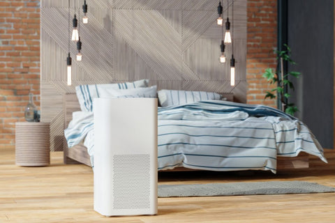 Modern white air purifier on a wooden floor in a contemporary bedroom with striped bedding and industrial-style lighting