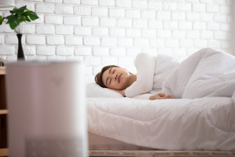 benefits of sleeping with air purifier - close up view of air purifier with woman sleeping in the background