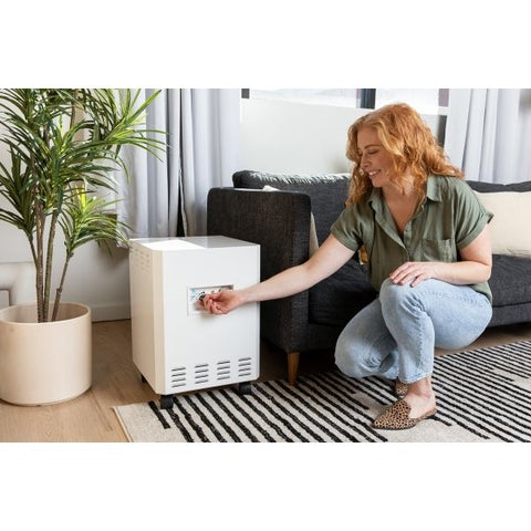 Woman in a modern living room turning on the EnviroKlenz Air System Plus, the best air purifier for cigarette smoke, next to a potted plant and striped rug.