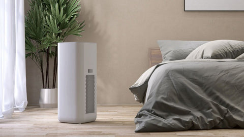 best air purifier for copd sitting next to a bed in front of a plant