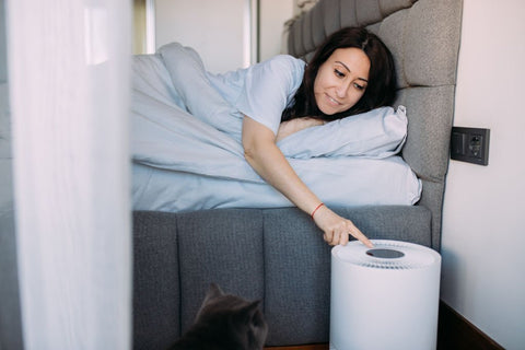 do air purifiers help with congestion -  woman on couch reaching down to turn on air purifier