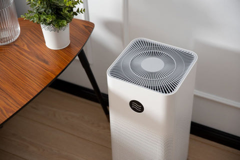 White air purifier sitting next to a wood table answering the question: "How to know if you need an air purifier"