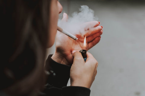 Woman lighting a cigarette, with second-hand smoke highlighting the need for an effective air purifier in the vicinity