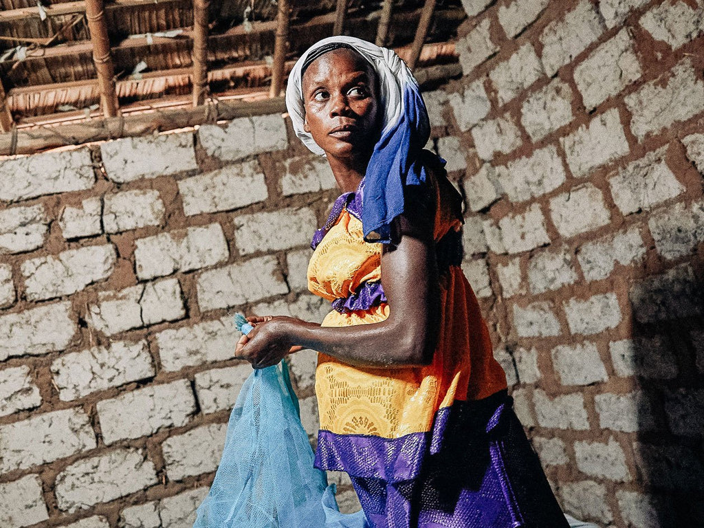 Congo Woman holding Mosquito net in a mud hut