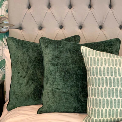 Forest green velvet and sage patterned pillow gifts against a taupe headboard