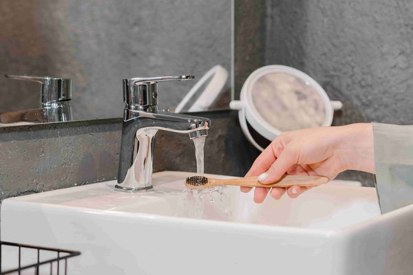 a hand holding a toothbrush at the sink for washing brush head