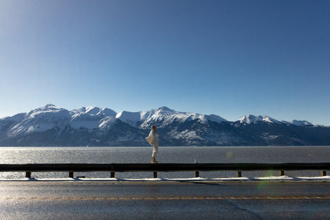Musician Quinn Christopherson standing on top of a highway guardrail against the backdrop of snowy Alaskan mountains.