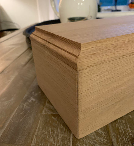 Oak box with a natural finish sitting on a rustic coffee table. The angle of the picture accentuates the tightly fitted corner and beveled boxtop.