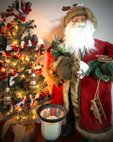Small Christmas tree decorated with handturned wooden ornaments in natural and gold leaf finish, standing next to Santa wearing a red robe, fur hat, and holding a small sleigh with white birds in his hands.