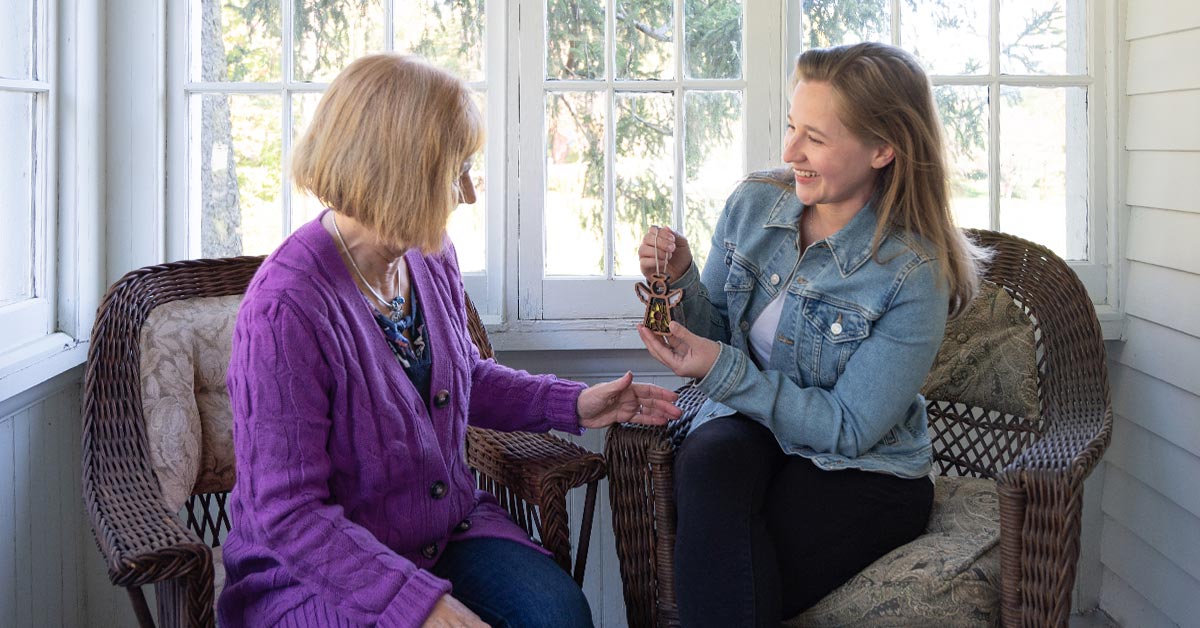 Daughter gifting Mother’s Angels® ornament to her smiling mom, perfect Mother's Day gifts, in a sunny porch setting, epitomizing heartfelt gifts for mom.