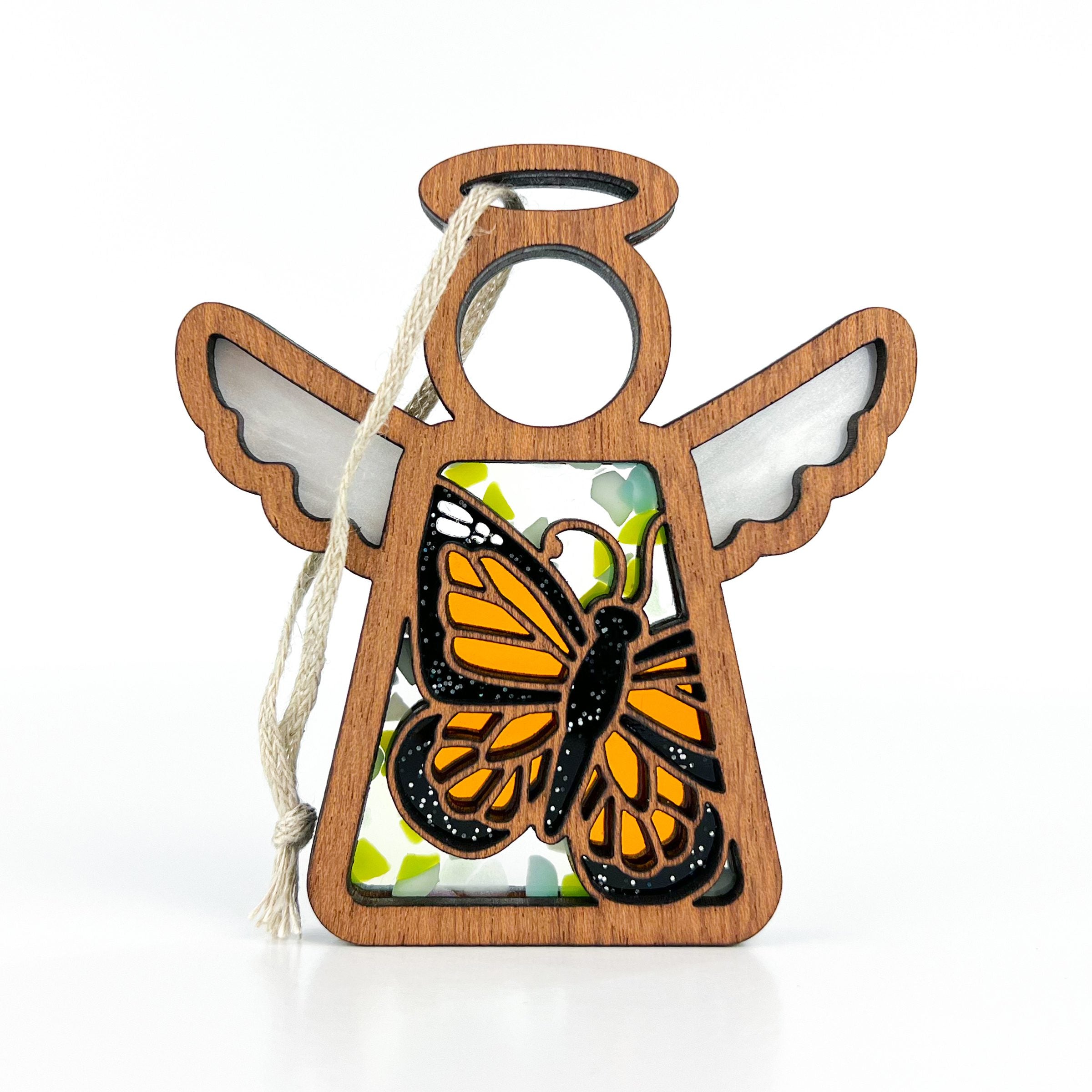 This Mother’s Angels® Monarch Butterfly Ornament embodies the awe-inspiring journey of the monarch butterfly migration. The handcrafted ornament features a vivid orange and black monarch butterfly design, reminiscent of stained glass, set within a wooden angel-shaped frame, complete with delicate white wings and a loop for hanging. The interplay of colors and light brings the magic of the migration into your home.