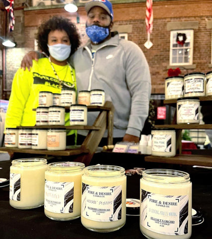 Les fabricants de bougies de Fire & Desire Candle Co. s'embrassent pour la photo derrière une table présentant leurs bougies