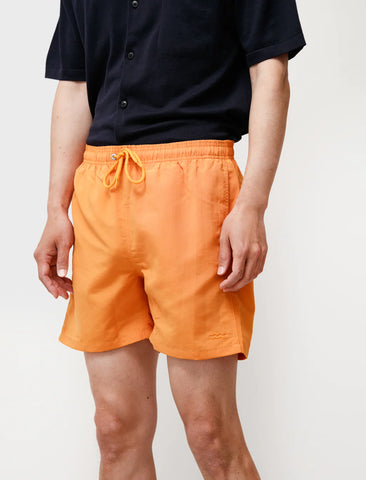 Man wearing an orange pair of Hauge swim trunks by Norse Project