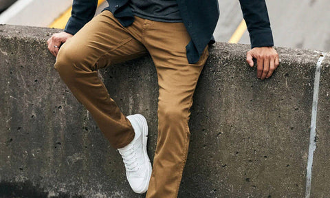 Close up of DU/ER No Sweat pants on a person leaning against a concrete block