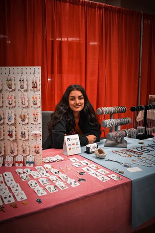 Norm, the owner of Norm's Niche, sitting at a vendor table at a market with her earrings, bracelets and necklaces on display