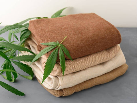 A stack of hemp shirts on a grey table with hemp leaves scattered across the bottom left of the stack