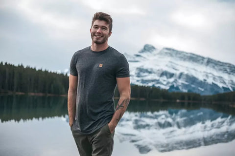 Man wearing a Tentree hemp shirt walking by a lakeside with a mountain behind him