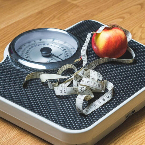 weight loss scale with measuring tape and an apple