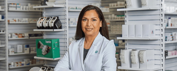 Employee mental health and how holistic pharmacy can help - A pharmacist smiles at the camera while standing in front of a shelf of medications