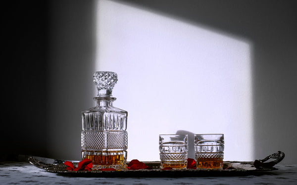 A crystal decanter and two matching glasses, each containing a translucent brown liquor