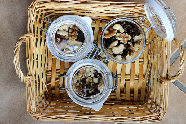 Letter vitamins: Three reusable jars containing a variety of raw nuts sitting in a basket. One jar is open to reveal contents, the other two are sealed.