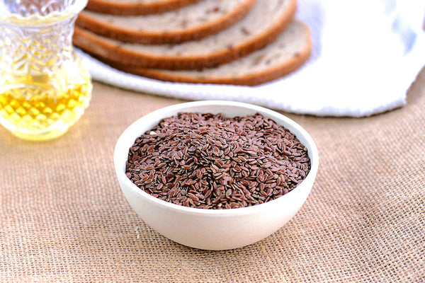 Letter vitamins: Unmilled flax seeds in a white bowl on a rustic tabletop with wholegrain bread in the background