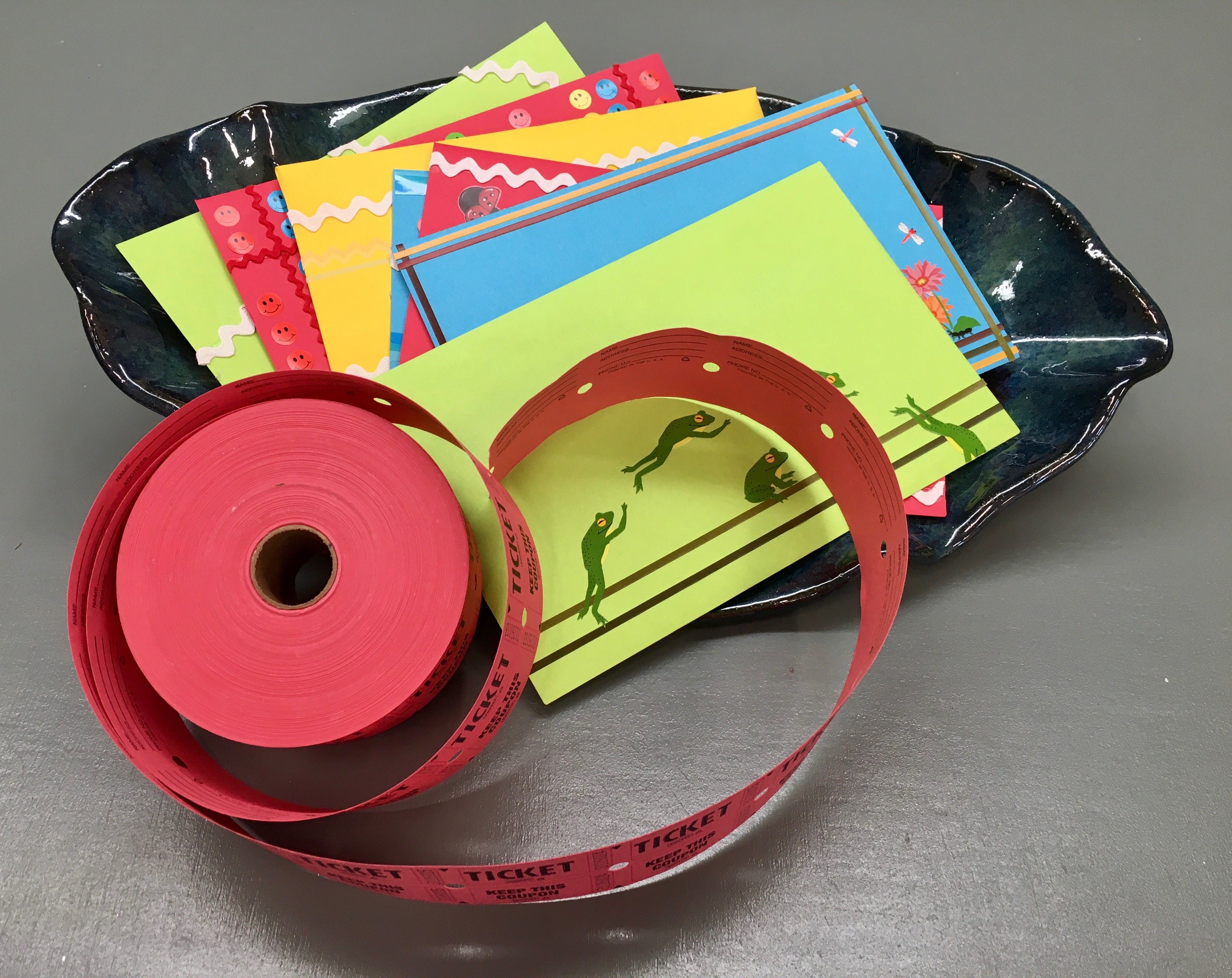 a scallop shaped ceramic bowl full of colorful envelopes and a spool of red raffle tickets