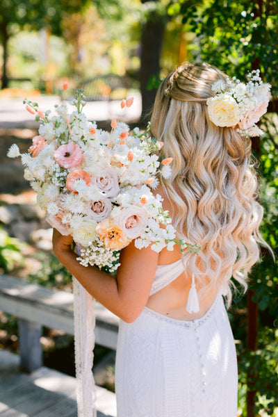 bride with blonde hair holding white bouquet that has pops of pale orange flowers