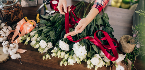 girl holding red ribbon with white flowers on the table arranging with care