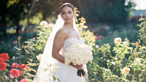 bride in field holding all white rose bridal bouquet in her hand