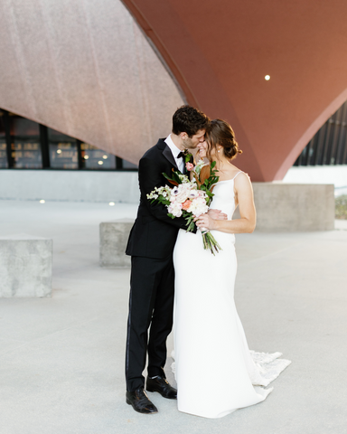 bride holding bridal bouquet with groom kissing brides face