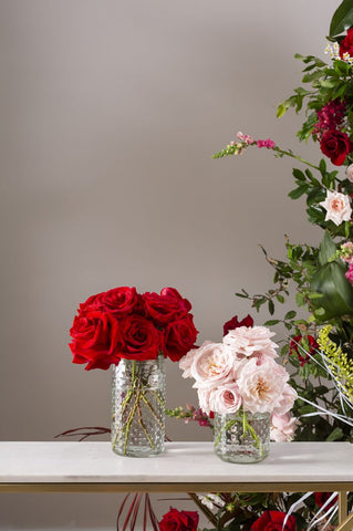 red and pink roses in two various sized vases on a white table