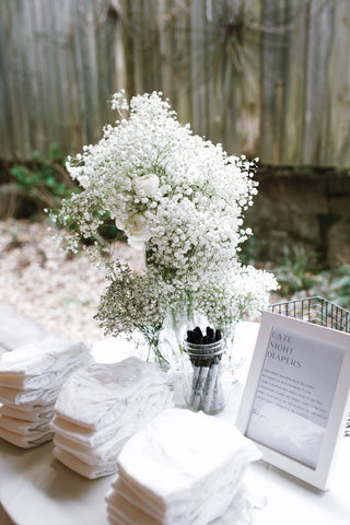 white baby shower table with white diapers and white flower arrangement