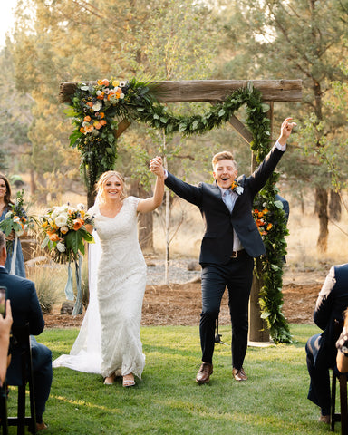 bride and groom walking away from wedding floral garland arch and alter