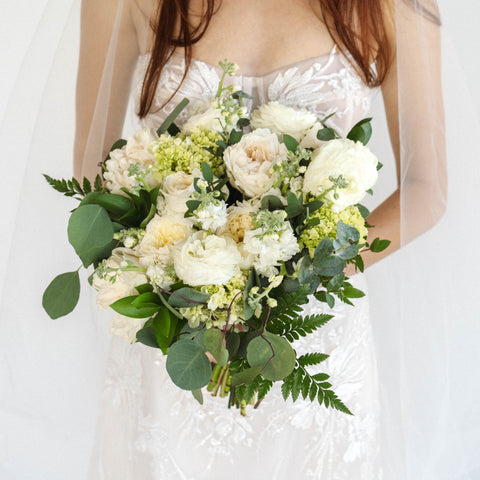 bride with red hair holding bridal bouquet with white roses and other white flowers and greenery