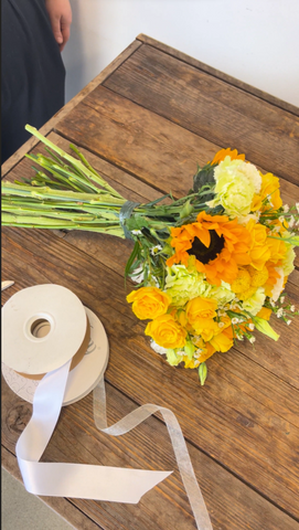yellow bouquet on a wooden table next to a white ribbon