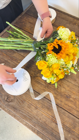 someone measuring a white ribbon around a yellow flower bouquet