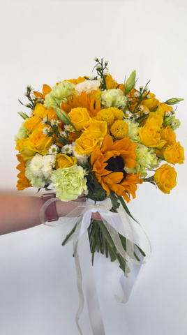 yellow bouquet wrapped in white ribbon in front of a white wall