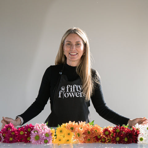 liza roeser standing in front of a row of rainbow daisy flowers