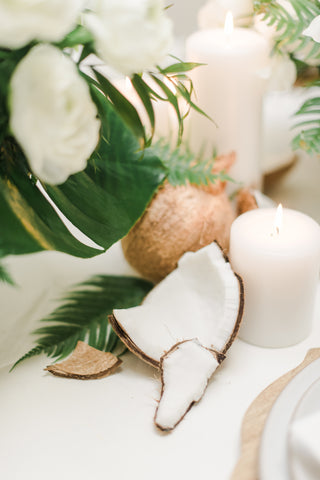 coconut husk on a table surrounded by a white candle and some greenery