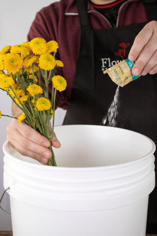 man processing yellow flowers and pouring flower food into water bucket