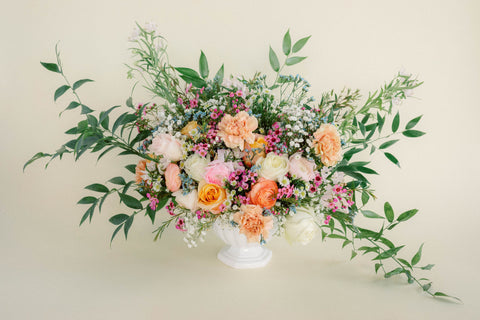 flower arrangement with pink and orange flowers with greenery in a white short vase