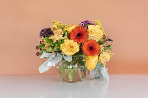 small round centerpiece with yellow and orange flowers on a white table in front of a orange wall